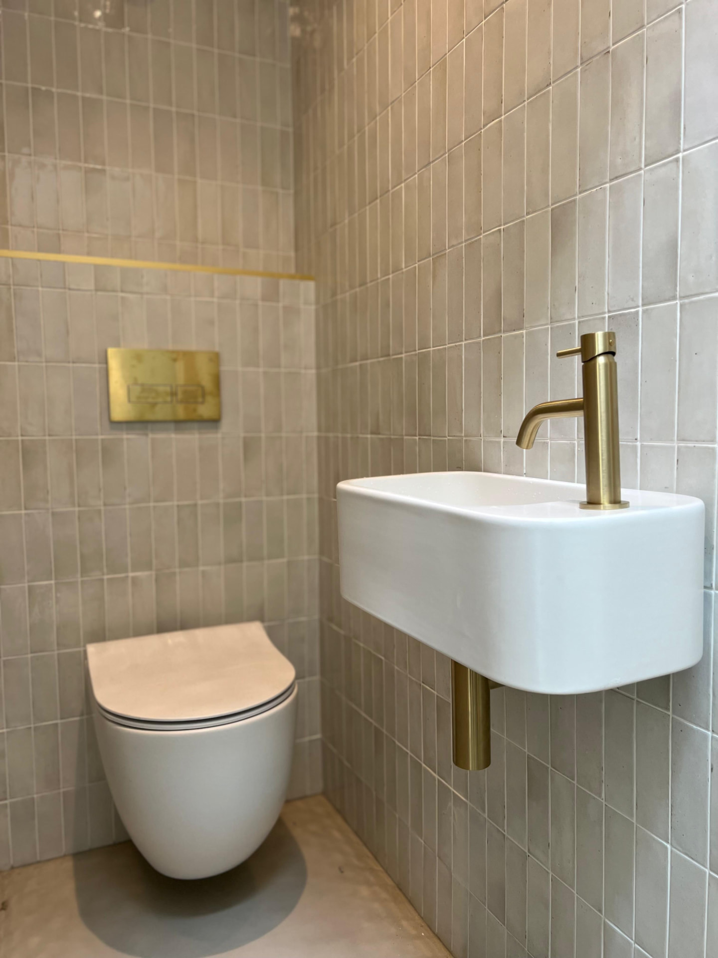 Wall-hung basin and toilet with brushed brass fittings in a tiled cloakroom