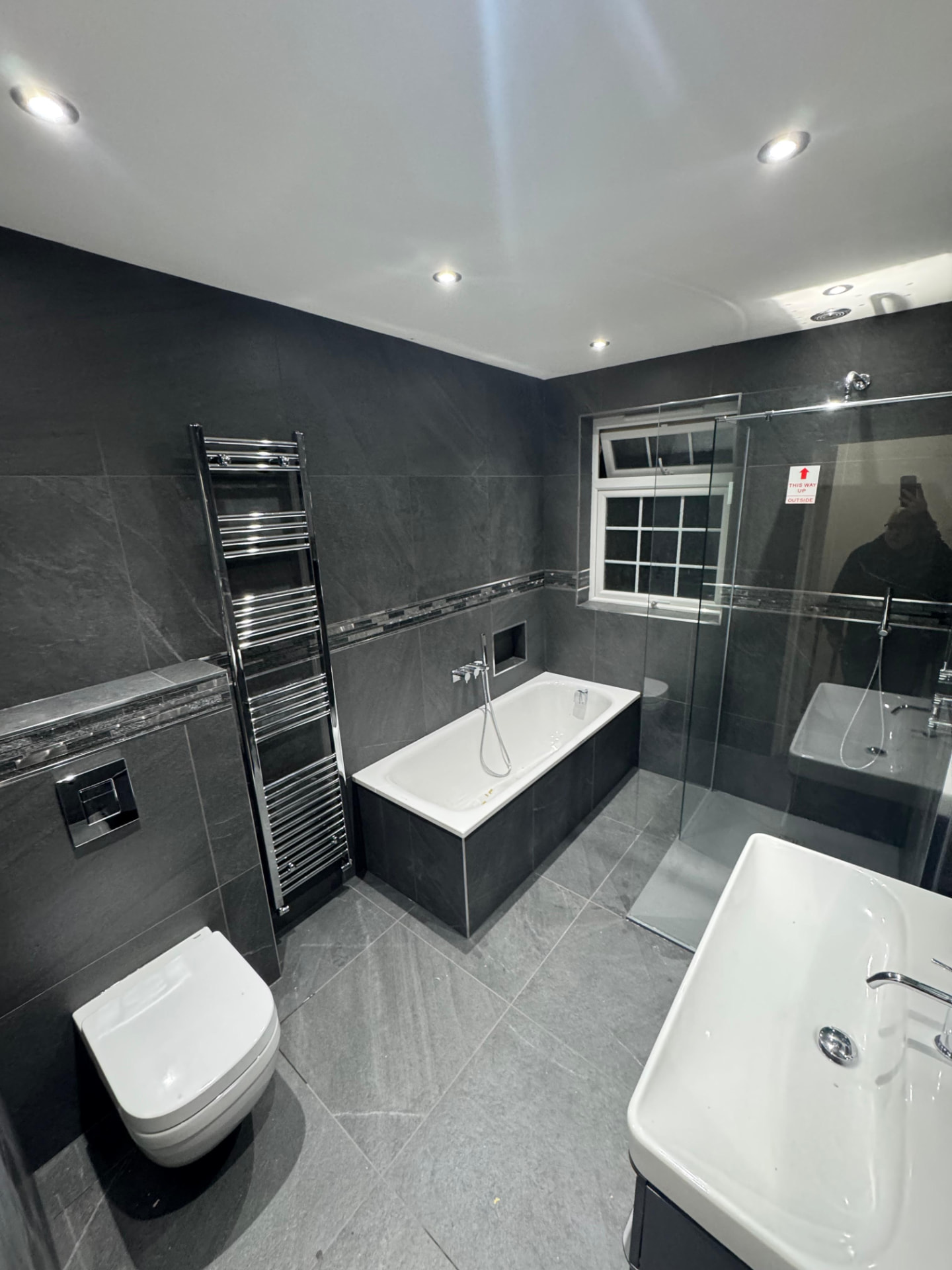 Grey tiled bathroom with bath, walk-in shower and chrome towel radiator