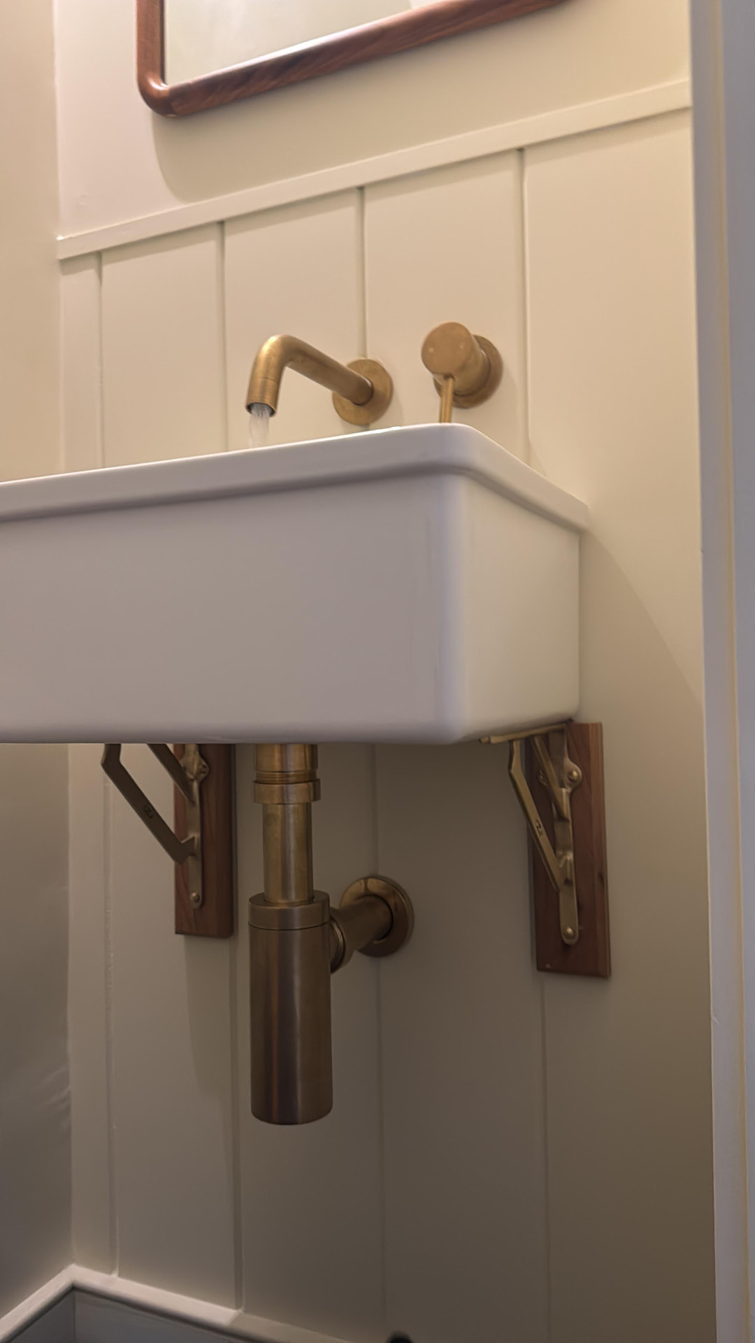 Wall-mounted basin with aged brass tap and exposed brass bottle trap
