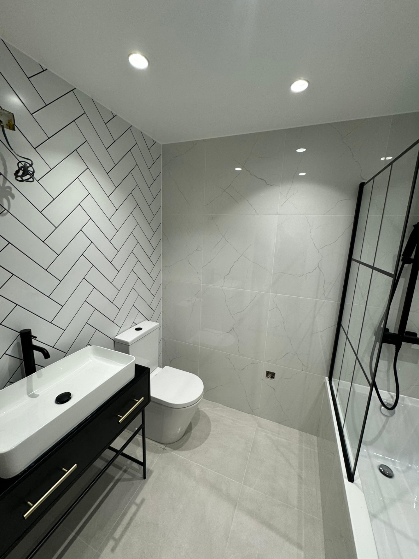 Completed bathroom with herringbone tiling, black framed screen and vanity basin